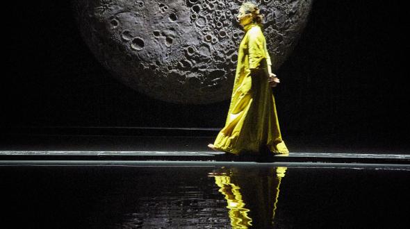 Théâtre - Les messagères - Une femme passant devant une lune sur scène 